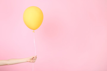 Female hand holding yellow balloon on pink background
