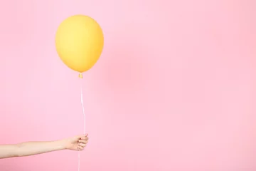 Schilderijen op glas Female hand holding yellow balloon on pink background © 5second