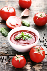 Ketchup in bowl with basil leafs and pepper on wooden table