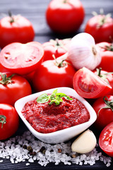 Ketchup in bowl with basil leafs and salt on black wooden table