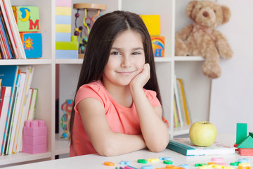 School activity, happiness and smartness.  Cute adorable child girl sitting by the table and smiling.