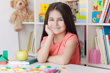 School activity, happiness and smartness.  Cute adorable child girl sitting by the table and smiling.