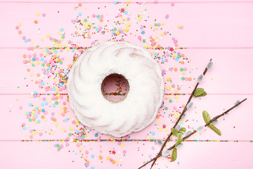Easter bundt cake with colorful confetti and willow branches on pink wooden table
