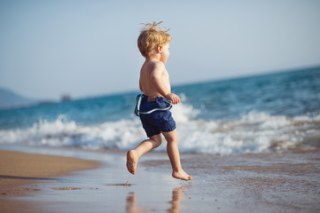 A small toddler boy with shorts running on sand beach on summer holiday.