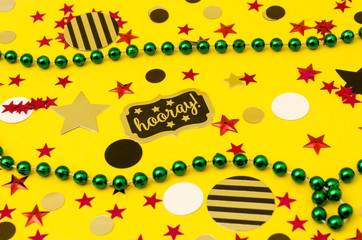 Top view decoration for party. Plastic green necklaces and circles and stars confetti on yellow background