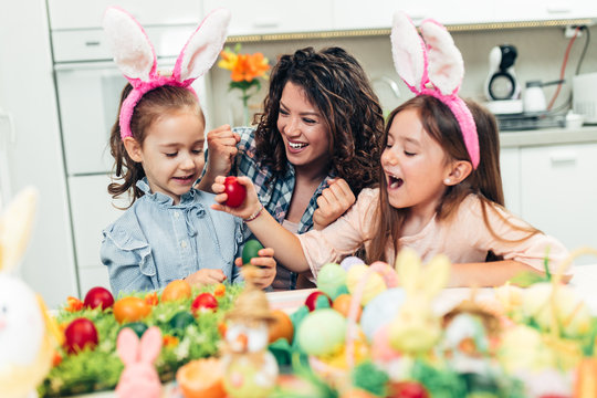 A mother and her cute daughters are painting eggs. Happy family are preparing for Easter. They are all wearing bunny ears.