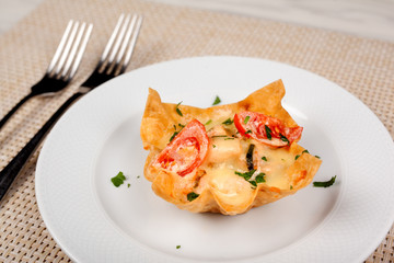 Snack with tomato baked in the dough with cheese on a white plate.