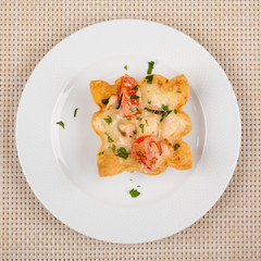 Snack with tomato baked in the dough with cheese on a white plate.