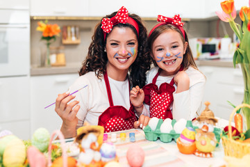 Mother and her cute little daughter having fun in kitchen while preparing Easter eggs.
