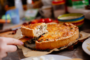 French quiche with cheese, spinach, mushrooms, bacon, dried tomatoes. French quiche on a plate only from the oven. A piece of cake on a paw. 