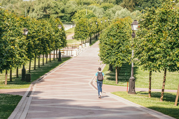 a young man with a backpack on his back, riding a scooter along a stone walkway of a large beautiful green park