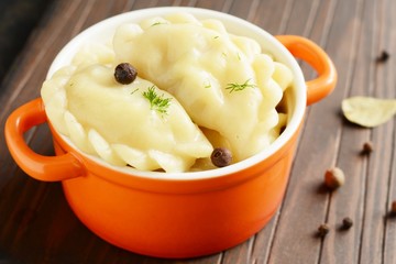 Dumplings with potatoes with herbs, spices and butter in a ceramic portion pot on a dark background. Varenyky, vareniki, pierogi, pyrohy - dumplings with filling.