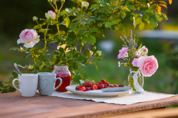 Morning tea in the garden. Fresh roses on wooden table, sunny day, natural ligh