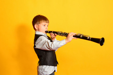 A little boy in a suit plays the clarinet - obrazy, fototapety, plakaty