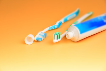 Two toothbrushes and a tube of toothpaste are close-ups on a yellow background in the studio