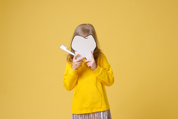 Little cute girl with toothbrush and dental layout in hand isolated on yellow background. Concept of health, oral hygiene, people and beauty. Layout of the space. Selective focus.