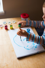 Left hand toddler drawing brush with gouache paint on paper in an album with several colorful...