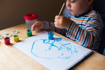 Left hand toddler drawing brush with gouache paint on paper in an album with several colorful...
