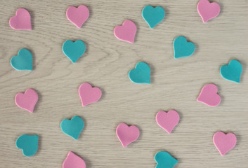 Fototapeta premium Small hearts of pink and blue color lie on a white wooden table.