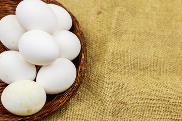 White chicken eggs in wicker basket on sackcloth background
