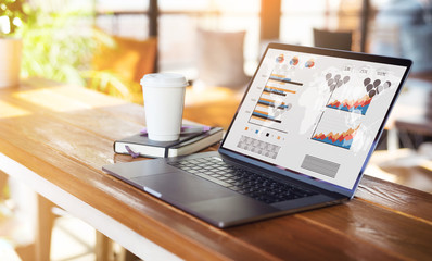 Close up of laptop with graphs, charts on screen,cup of coffee on table in empty room, cafe. Computer on wooden desk.