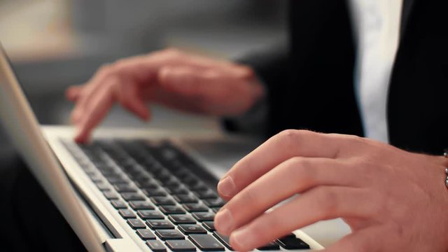 Close up shot of male hands typing on laptop keyboard with city street on the background. Businessman typing text