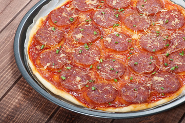 Pizza with salami and cheese on the old wooden background.