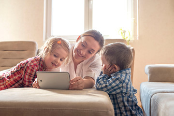 Mother with children watching cartoons on tablet and having fun together at home