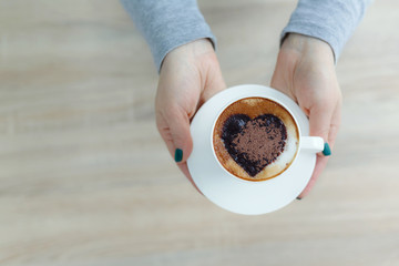 Top view hands holding white cup of coffee. heart print on coffee