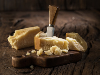 Piece of Parmesan cheese and cheese knife on the wooden board. Dark background.