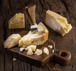 Piece of Parmesan cheese and cheese knife on the wooden board. Dark background.