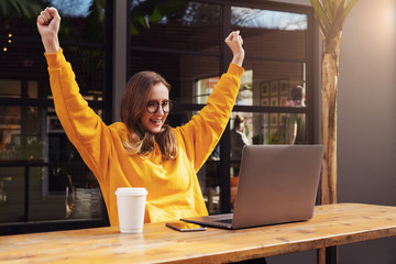 Girl rejoices in winning having raised her hands up sitting in front of laptop.Woman watches sports...