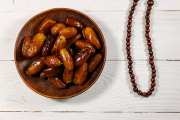 Dates fruit and rosary on white wooden table. Top view
