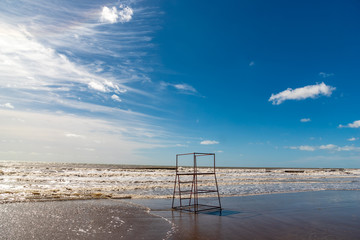 Empty beach in Argentina with high tide with a red lifeguard stand made of tubes with some clouds