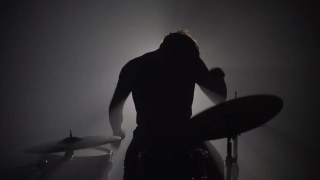 Silhouette of male drummer playing drums in dark