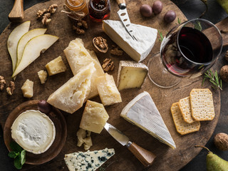 Cheese platter with different cheeses, fruits, nuts and wine on stone background. Top view. Tasty cheese starter.