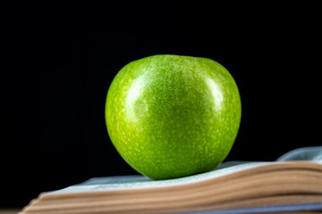 Open book and a green apple in front of black background