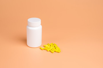 Yellow pills, tablets and white bottle on orange background.