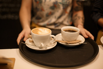 Woman bring two white cups of latte and americano coffe on tray