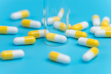 Medicine white and yellow pills or tablets drop out of the test tube on blue background