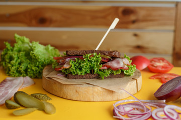 juicy sandwich with grilled dark bread and bacon wait for you on wooden plate