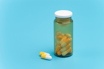 White and yellow pills, tablets and brown glass bottle on blue background