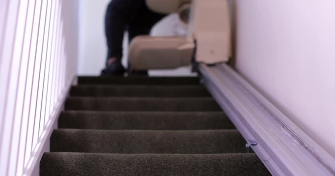 Senior Woman Sitting On Stair Lift At Home To Help Mobility