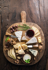 Cheese platter with organic cheeses, fruits, nuts and wine on wooden background. Top view. Tasty cheese starter.
