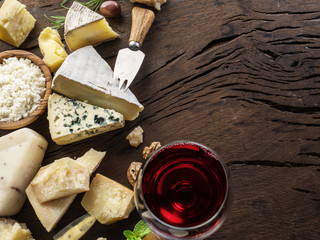 Cheeses with organic cheeses, fruits, nuts and wine on wooden background. Top view. Tasty cheese starter.