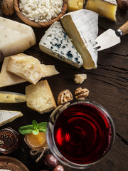 Cheese platter with organic cheeses, fruits, nuts and wine on wooden background. Top view. Tasty cheese starter.
