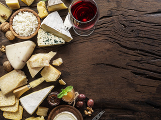 Cheese platter with organic cheeses, fruits, nuts and wine on wooden background. Top view. Tasty cheese starter.