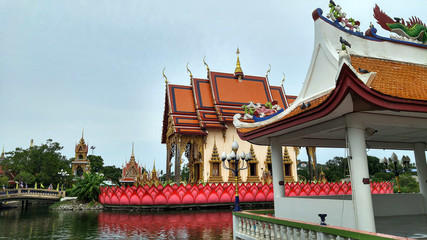 Fototapeta na wymiar Asian style buddhist temple standing on the lake. Multi colored buildings and a bridge leading inside.