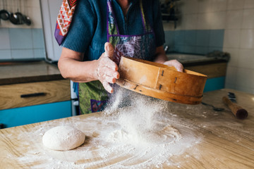 Grandmother cooking, hands of old woman sifting flour through a sieve  onto dough. 