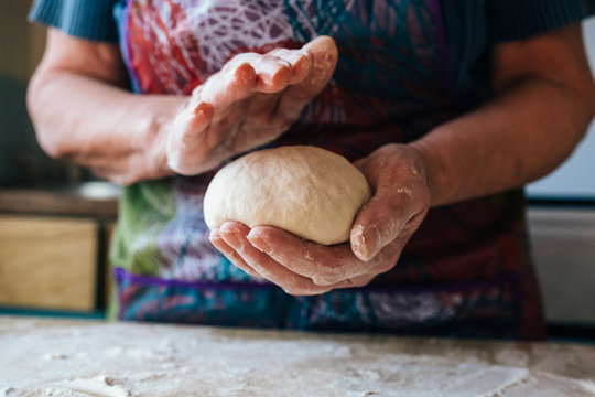Wrinkled grandmothers hands holding and kneading fresh bread dough